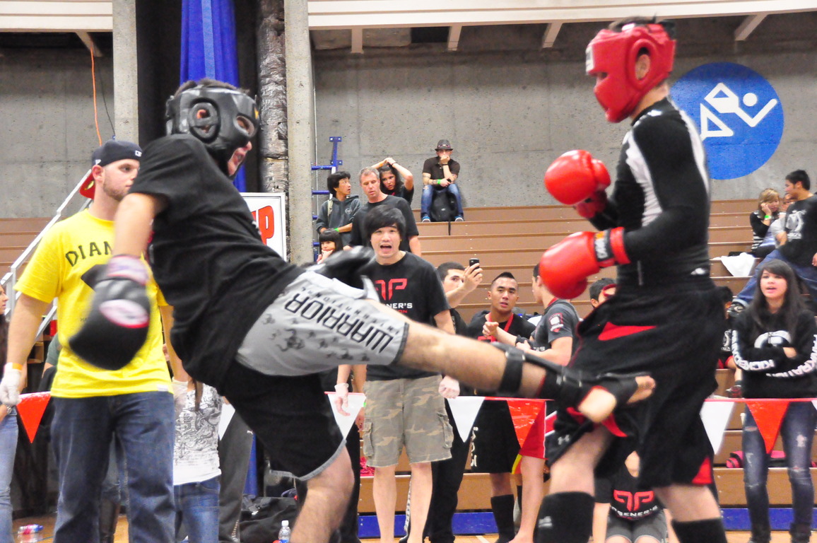 Two athletes in protective equipment exchange a low kick in amateur Muay Thai.
